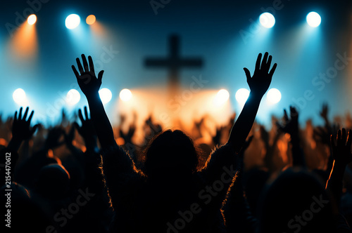 people raising their hands in worship at a church, with a cross on the stage background	
