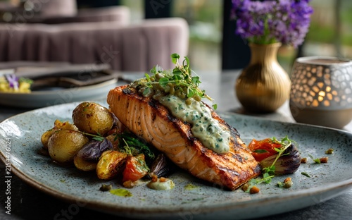 grilled salmon fillet with creamy herb sauce, roasted baby potatoes and vegetables served as an elegant gourmet restaurant meal