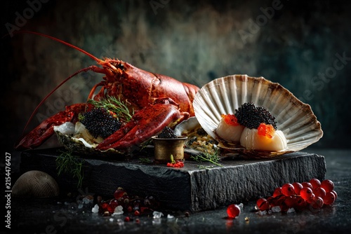 luxury seafood still life with lobster, scallops, oysters and black and red caviar served on dark stone with dramatic fine dining presentation