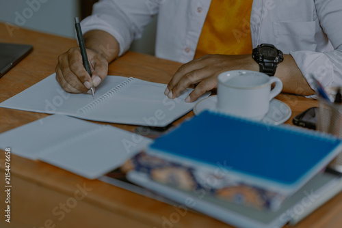 Student hands writing notes with pen in notebook and laptop while studying from textbook at home. Close up. Learning, exam and education concept.