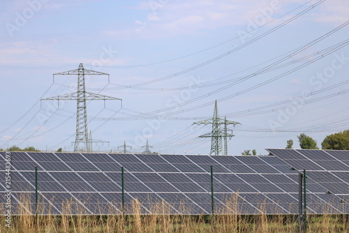 Canvas Print Solar panels in the foreground with high voltage transmission power pylon and ru