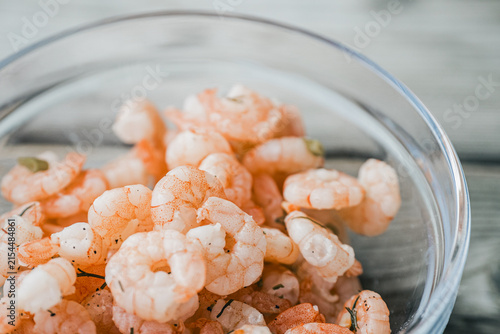 Konstfotografi Cooked pink shrimp seasoned with herbs and pepper fill a clear glass bowl, photographed in soft natural light with generous copy space in the upper right