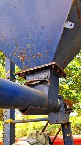 Rusty Blue Hopper and Screw Conveyor of an Agricultural Rice Mill Machine in a Sunny Farm Setting