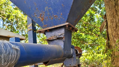 Heavy-Duty Agricultural Machinery: Rusty Blue Metal Hopper and Screw Conveyor System for Rice Milling and Grain Processing in a Rural Farm Setting