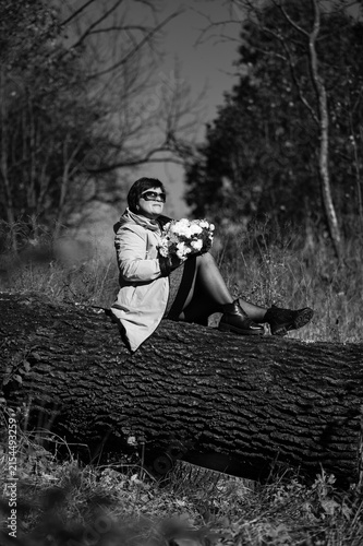 Obraz na plátně Woman sitting on a log in a serene forest, holding a bouquet of flowers with a j