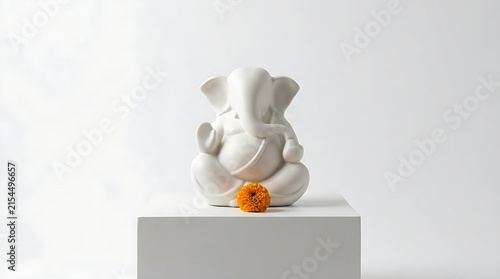 Minimalist white Ganesha statue displayed on a pedestal with an orange marigold flower, creating a peaceful spiritual scene with clean studio lighting and copy space