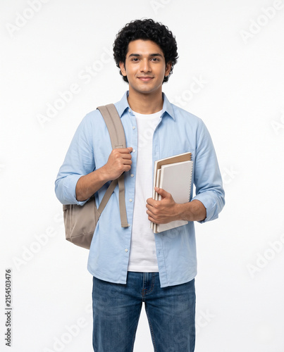 Young Indian male student in sky blue shirt holding books and backpack while smiling confidently isolated on white for study abroad education