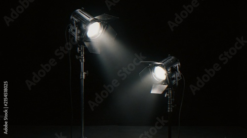 Cuadro en lienzo Two studio lights set up on tripods against a dark background, with beams of light illuminating the space