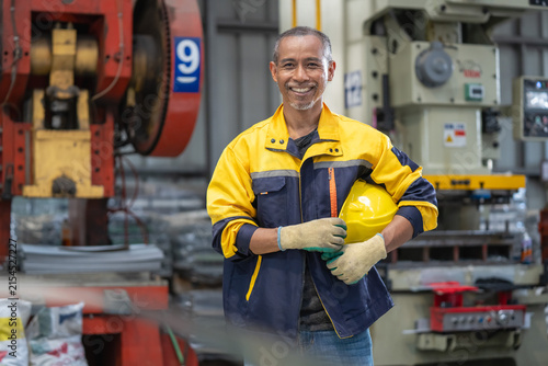Cheerful factory employee wearing safety equipment and holding a hard hat in an industrial setting