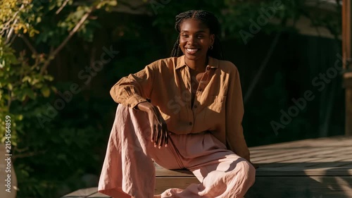 Woman in linen shirt and wide pants seated on wooden steps in soft golden light for boho lifestyle portrait background and editorial use