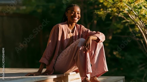 Sunlit portrait of a woman in a relaxed pose on deck steps surrounded by greenery for wellness background and calm lifestyle design