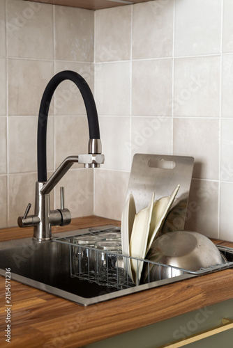 Kitchen with stainless steel sink and contemporary black faucet, dishes and cutlery being washed by hand, neatly stored in dish rack. Manual dishwashing, organization, practical storage, modern design