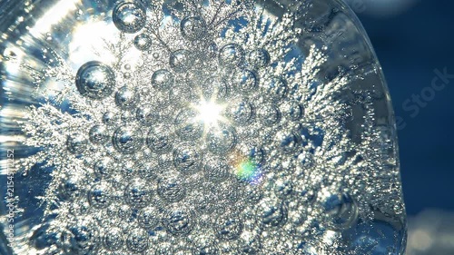 Clear ice sphere with intricate frozen patterns and bubbles reflecting sunlight, showcasing the beauty of winter in a close-up view against a blurred blue background