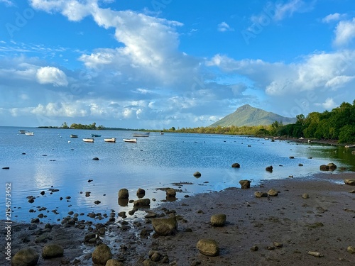 : Calm lagoon at low tide with small boats and a mountain on the horizon — horizontal