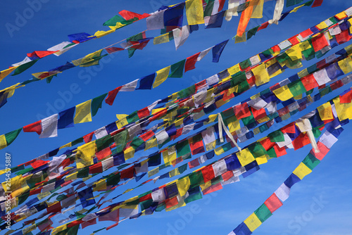 Colorful Tibetan Buddhist prayer flags fluttering against a clear blue sky, symbolizing peace, compassion, spirituality and Buddhist tradition