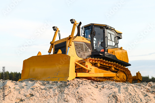 Modern bulldozer working on sand at a quarry or construction site. Heavy machinery moving and leveling sand during earthmoving and industrial operations.