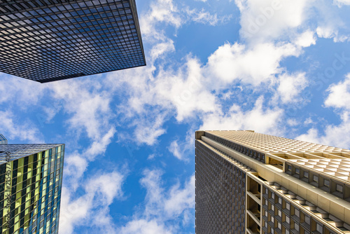 Low angle wide perspective looking up at historic and modern Manhattan skyscraper facades against blue sky with clouds in New York