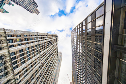 Low angle wide perspective looking up at historic and modern Manhattan skyscraper facades against blue sky with clouds in New York