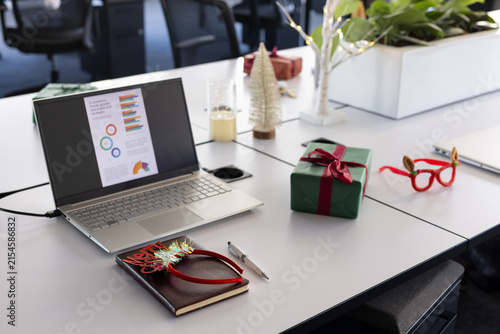 Silver laptop is displaying business chart on white desk with green gift and decorations at office