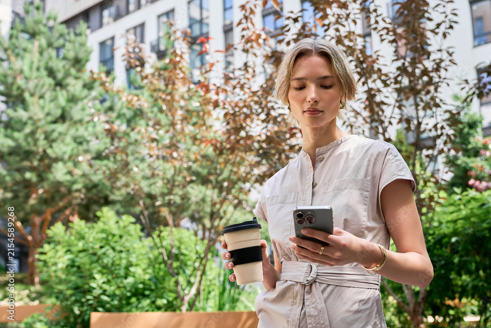 Fototapeta premium Stylish woman enjoys coffee and checks phone in vibrant city setting