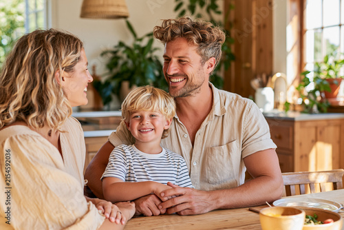 A cheerful family of three including a mother father and young son share a loving joyful moment while sitting together at their home dining table