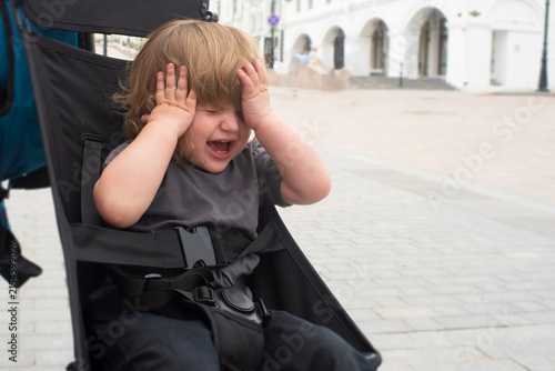 Sad toddler boy crying and having tantrum inside stroller outdoors
