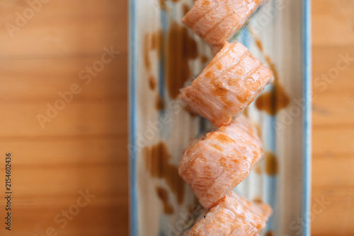 Four sushi rolls with salmon on a rectangular plate, drizzled with sauce.