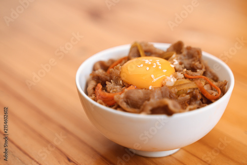 Gyudon rice bowl with thinly sliced beef, vegetables, and a raw egg yolk on top.
