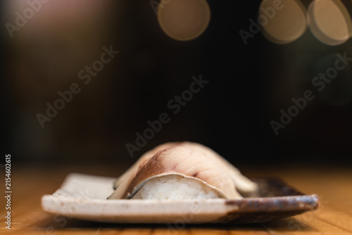 Two pieces of saba (mackerel)  sushis placed on a rustic ceramic plate, captured with a blurred and dramatic background.