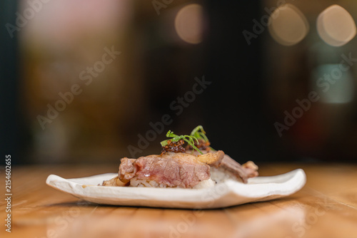 Side view of wagyu beef sushi with sauce and garnishes, elegantly plated on a white ceramic dish.