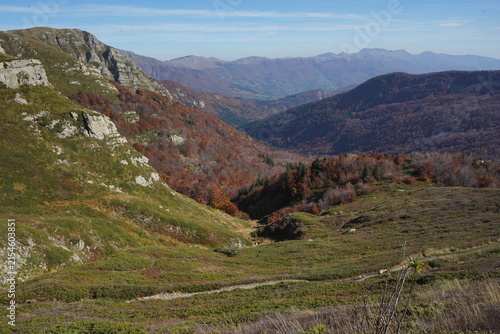 View of Lago Nero in the Apennine Mountains, surrounded by autumn-colored forests, rocky slopes, and mountain ridges under a clear blue sky in Abetone Cutigliano, Tuscany, Italy.