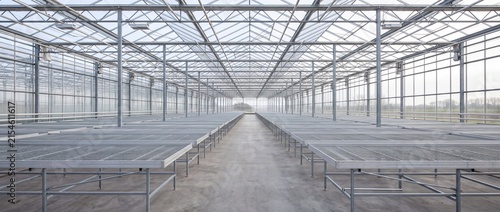 Empty modern commercial greenhouse interior with long metal growing tables and glass roof structure designed for advanced plant production