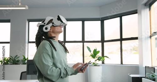 Non-binary African in white VR headset, mint top, looking up, tapping tablet testing VR in office
