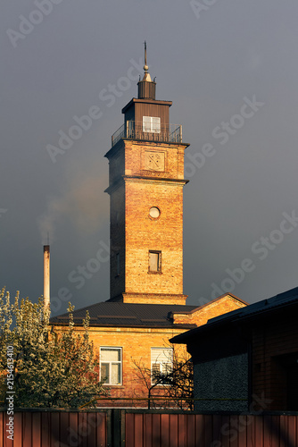 Historic brick tower illuminated by evening sunlight beneath dramatic gray stormy sky