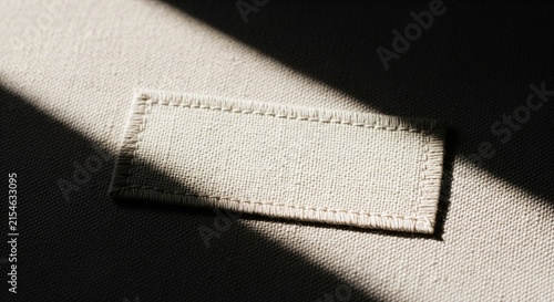 Empty fabric label stitched onto canvas textile, blank rectangular clothing tag for branding, minimal aesthetic macro photograph