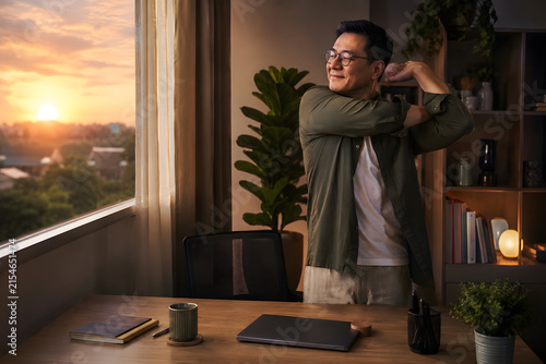 Man stretching in home office at sunset