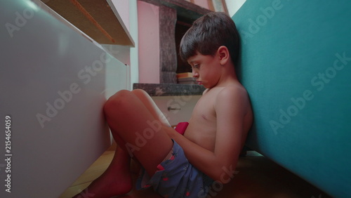 Принти на полотні Angry boy hiding behind sofa at home, withdrawn stare expressing frustration, mi