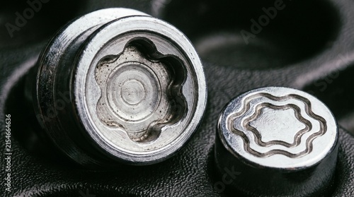 Macro shot revealing the intricate design of two metallic car wheel lock nuts, highlighting their anti-theft security features against a dark background.