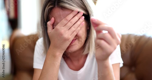 A woman sits thoughtfully in her cozy living room, experiencing a wave of emotions. She hides her face with her hands, deeply reflecting on her thoughts in the serene afternoon light.