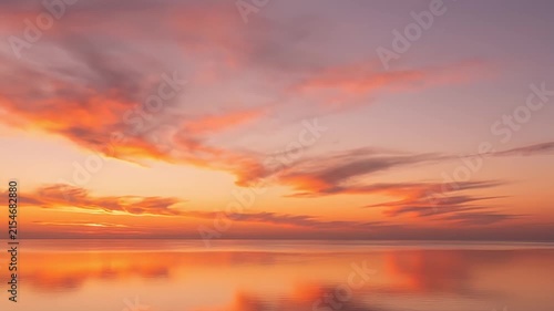 Tranquil sunset over calm ocean with pink clouds.