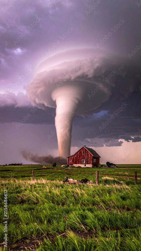 Obraz premium A dramatic, cinematic shot of a powerful tornado looming over a rustic red barn in an empty field. No people. This intense, atmospheric image evokes natures raw fury and resilience. Ideal for news.