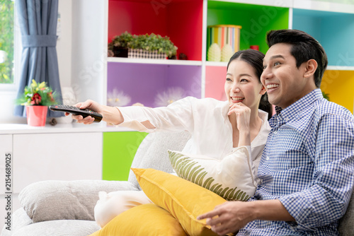 A young couple watches a sports game on television and cheers together in their living room at home.