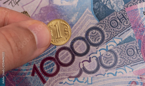 Obraz na płótnie A 1 Kazakhstani tenge coin held in a man's fingers against a background of 10000 tenge banknotes