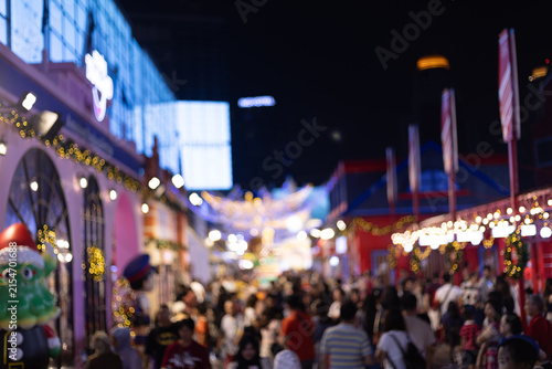 Crowded evening Christmas street market decorated with warm festive lights, colorful booths, and illuminated buildings, creating an energetic atmosphere for visitors and shoppers.