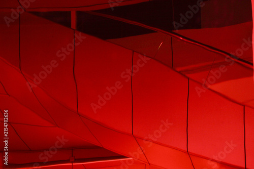 Abstract modern architectural dramatic red ambient lighting glowing across geometric wall panels cladding in a contemporary building interior.