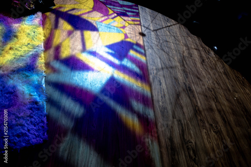 Colorful stained glass light casts vivid geometric shadows across a wooden floor, creating an atmospheric interior scene filled with vibrant patterns.