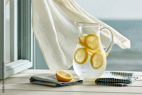 Glass pitcher of lemon water with a halved lemon and striped napkins