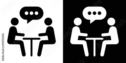 Flat vector symbol of two stick figures seated at a table communicating with a chat bubble, representing a one-on-one discussion or client meeting.