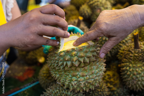 Customer touch fresh durian fruit from vendor, partially opened revealing yellow flesh