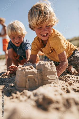 Zwei blonde Jungen bauen lachend gemeinsam Sandburg am Sandstrand